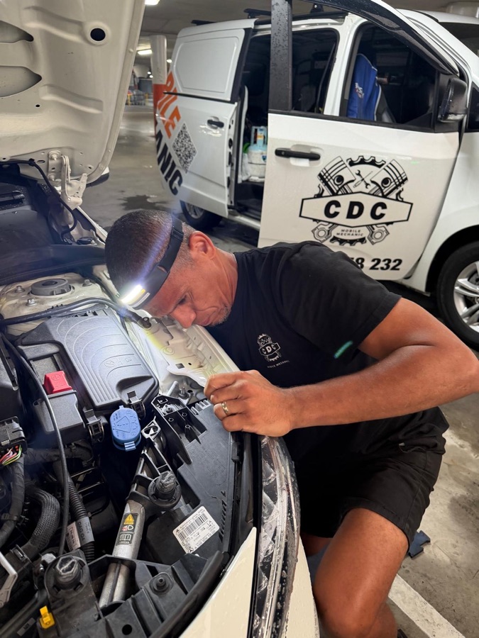 Carlos inspecting an engine bay with a head torch beside the CDC Mobile Mechanic van